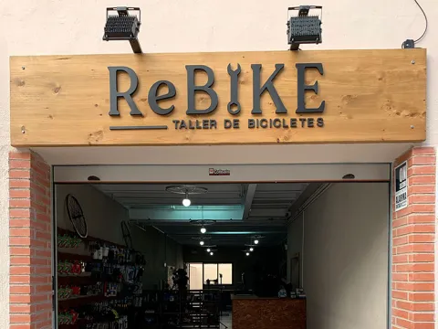  Rotulo de madera, logotipo en letra corpórea, iluminacion mediante dos puntos de luz Rebike tienda de bicicletas 